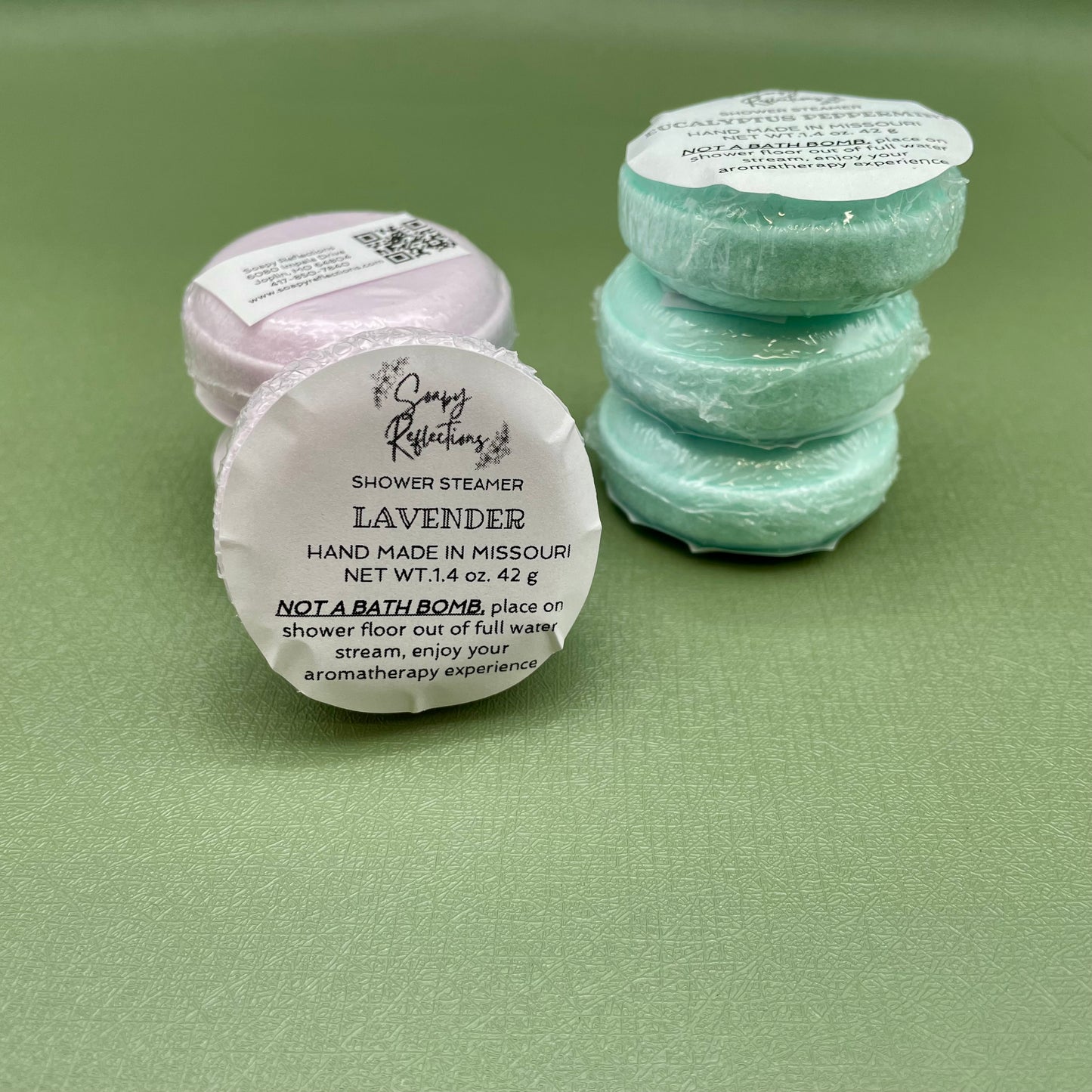 Six shower steamers in two stacks of three, one stack of purple, one stack of green.