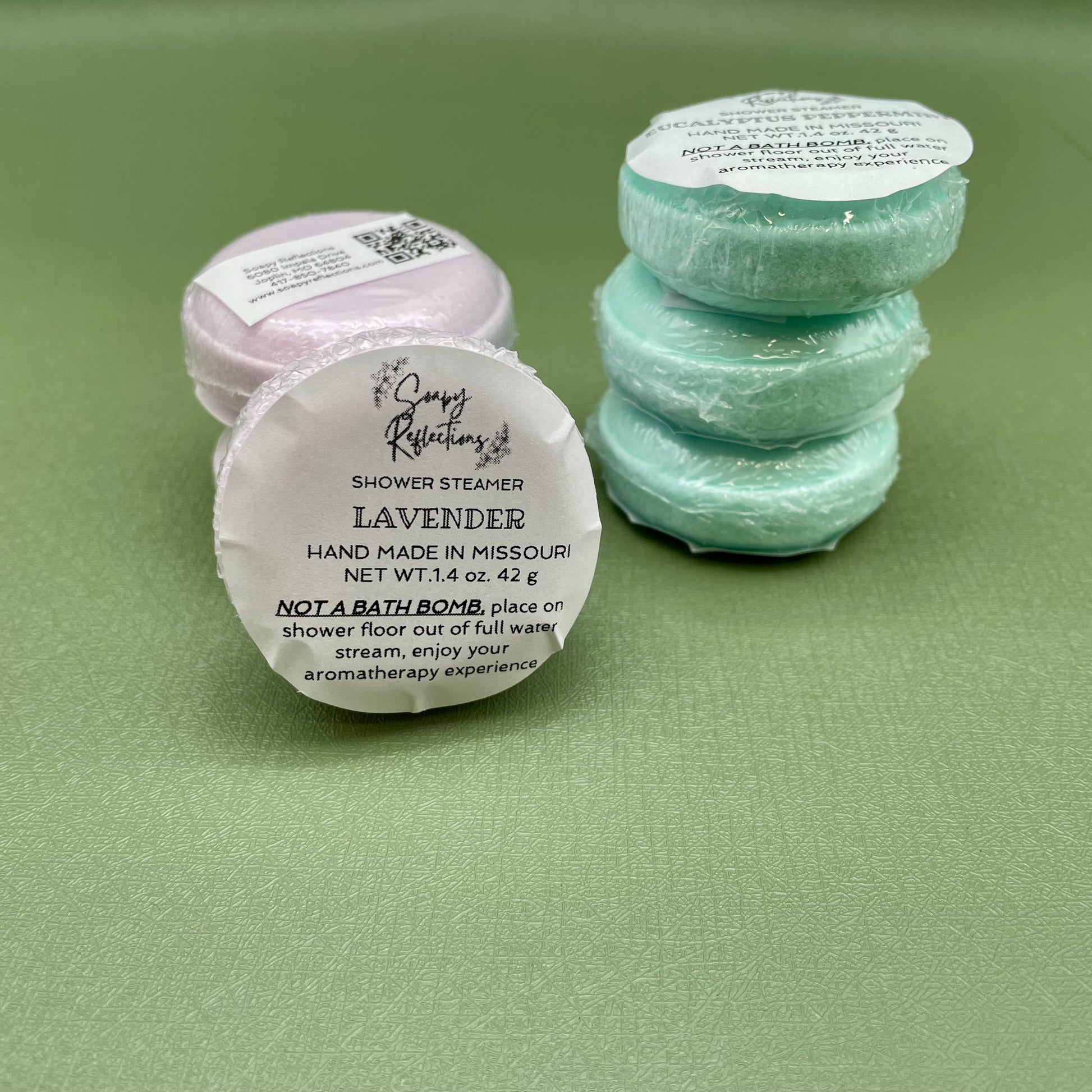 Six shower steamers in two stacks of three, one stack of purple, one stack of green. 