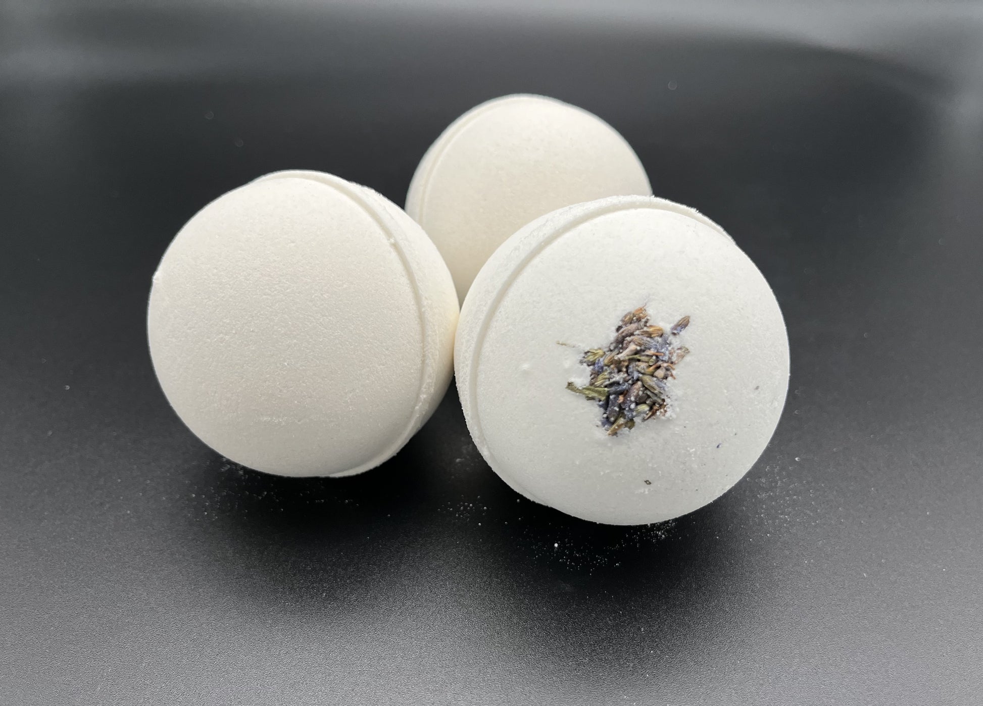 Three round white bath bombs, purplish brown  lavender buds imbedded in the bomb.