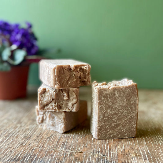 Stack of four soap bars, dark brown in color with white specks, vanilla bean scent. 