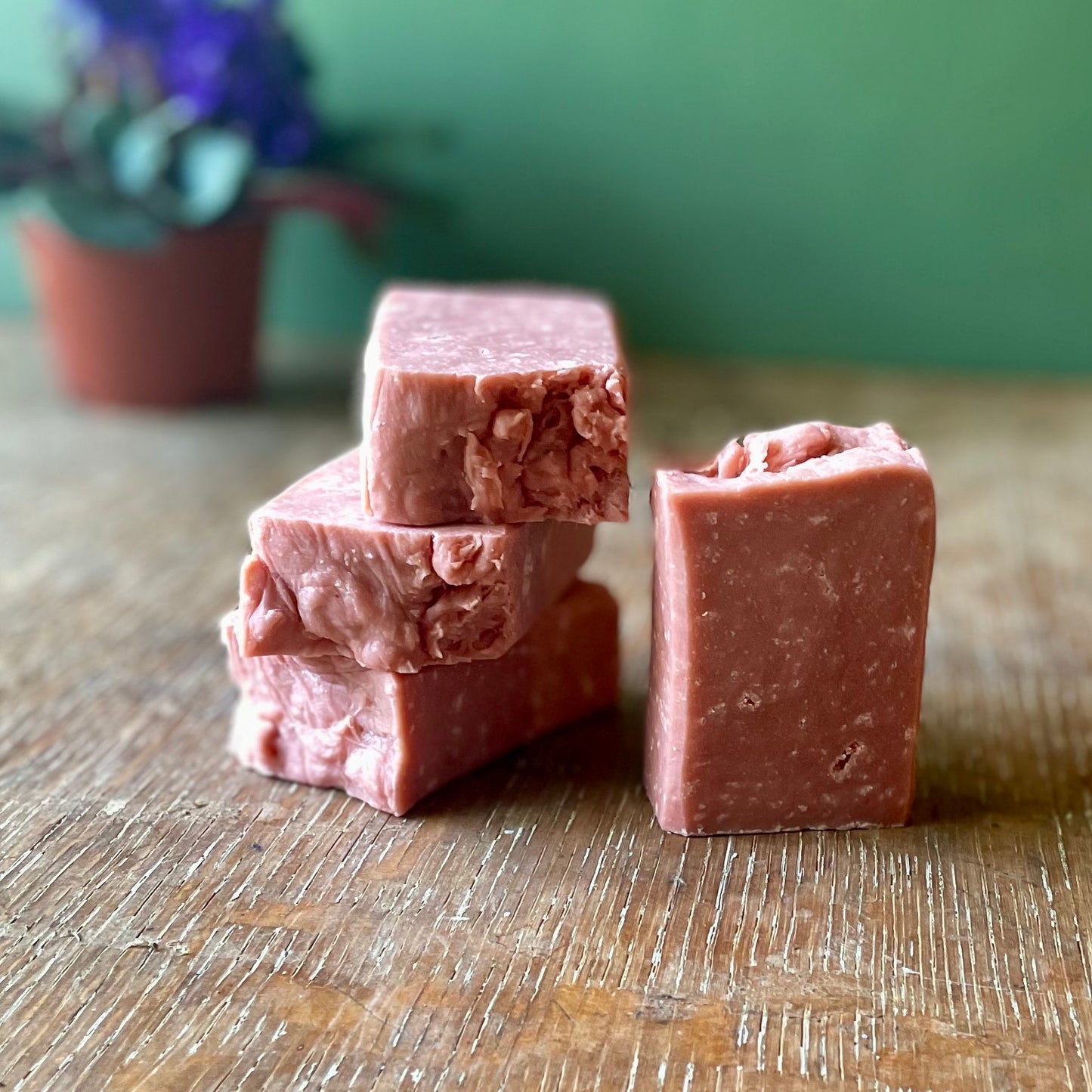 Stack of four soap bars, medium pink in color with white specks, strawberries and cream scent. 